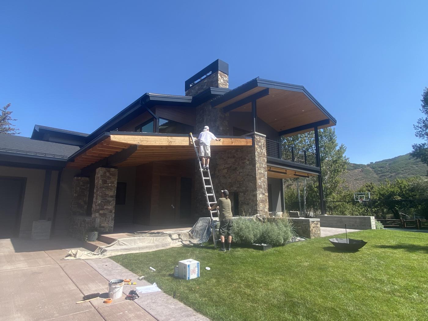 Painter on a ladder finishing a modern mountain home exterior